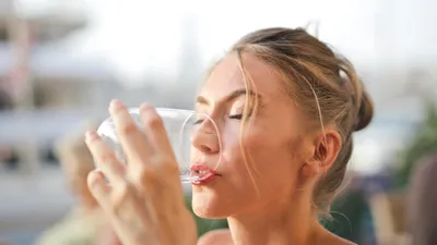Žena s blond vlasy pije vodu ze sklenice v letním prostředí restaurace